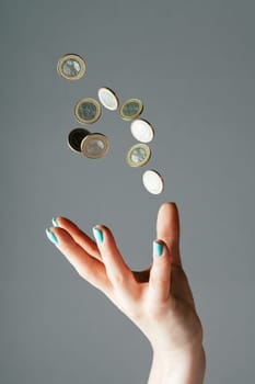 Female hand with blue nails throwing money, one euro coins into air on gray background. Levitating cash. Copy space, vertical
