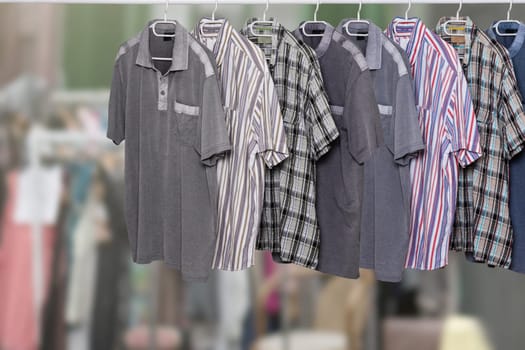 Clothes on rack. Clothing rack with various colorful male casual summer shirts over abstract blurred clothes shop. All hanging neatly on hangers at cloth rail. Space. Shopping.