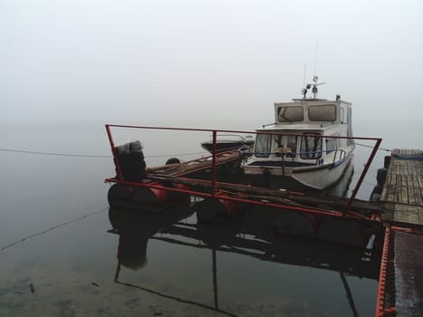 Belgrade, Serbia, January 14, 2020 White boat at the pier, left for the winter. Foggy weather on a January cloudy day. Reflection in the river river. House for shelter from the weather.
