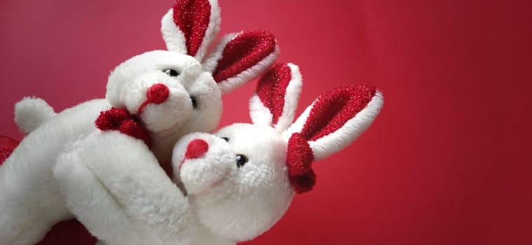 Two white plush rabbits cuddling. Dark red background. Children's toys are white. Greeting card on Valentine's Day. Mutual love and affection. Declaration of love.