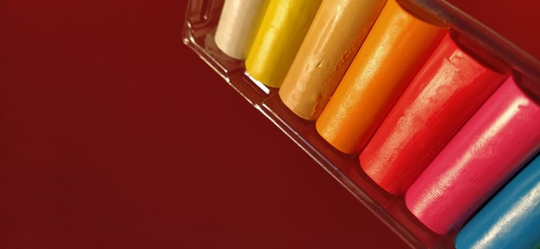 Multi-colored new plasticine in plastic packaging on a red background. Plasticine plates of red, pink, green, white, yellow, brown, blue, black. Set for children's creativity.
