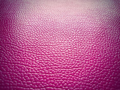 Artificial pig skin in bright pink or fuchsia. Grooves and elevations on the surface of a bag or shoe are clearly visible. Reflection of the light. Fashion accessory. Close-up. Light dark vignetting.