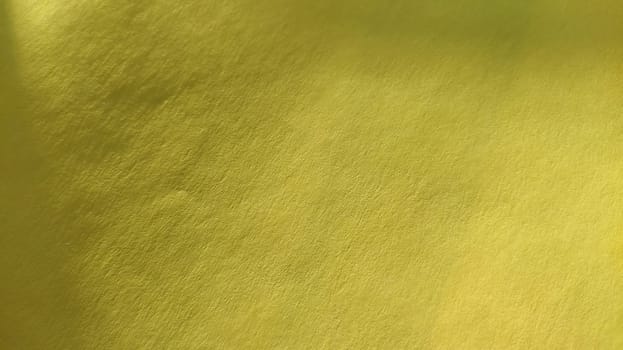 The paper or fabric material is bright yellow. Close-up. Slightly folded sheet. Light gradient and accentuated rough surface texture. Background or product sample. Sunny cheerful yellow.