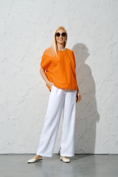 An adult woman in sunglasses posing in a stylish orange shirt and loose white trousers A fashionable portrait perfect for the summer season.