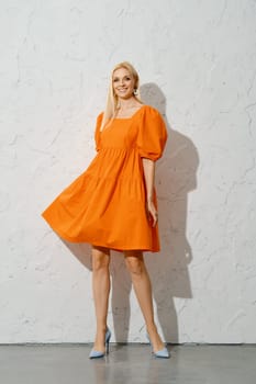 Cheerful adult woman waiving her orange dress and spinning on the spot