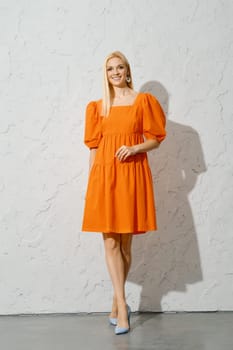 A smiling adult woman in a bright orange spring dress walking indoors, posing for the camera