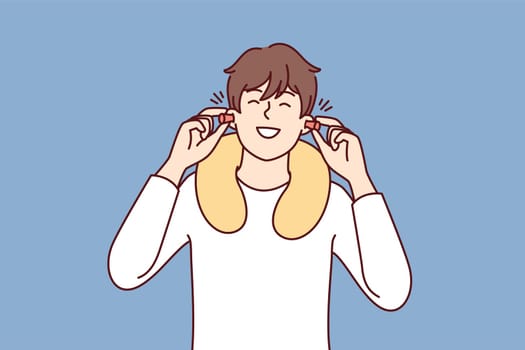 Happy man uses earplugs and neck pillow to rest during long journey on bus or plane. Positive guy traveler is in good mood after getting enough sleep on train