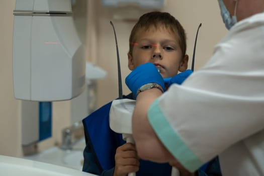 Jaw computed tomography, check up teeth in dental clinic. Boy in vest on x-ray diagnostics. Hands of radiologist in medical gloves do circular snapshot of jaw on modern medical equipment. CT scanning.