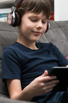 Portrait of happy little boy with digital tablet computer. Child in headphones play videogame on gadget or listen to music. Tablet in hands, home leisure, gamer, modern electronics.