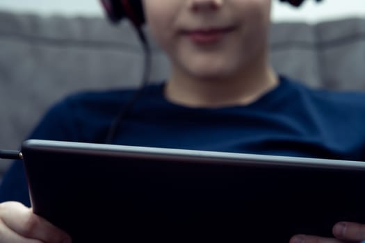 Portrait of smiling boy with digital tablet computer closeup. Child in wired headphones play videogame on gadget or watch video. Online entertainment, home leisure, gamer, modern electronics.