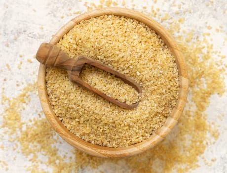 Raw Dry bulgur wheat grain in a wooden bowl with a scoop top view. Vegetarian and Vegan, Mediterranean and Middle Eastern cuisine. Healthy lifestyle