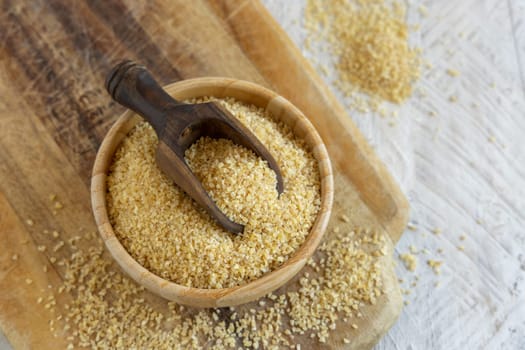 Raw Dry bulgur wheat grain in a wooden bowl with a scoop close up, copy space. Vegetarian and Vegan, Mediterranean and Middle Eastern cuisine. Healthy lifestyle