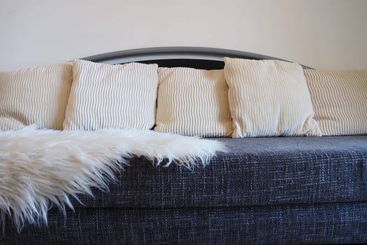 Gray sofa with rough upholstery fabric boucle and white decorative fluted cushions. A long pile white faux fur rug or coverlet is thrown over the seat. Living room interior.
