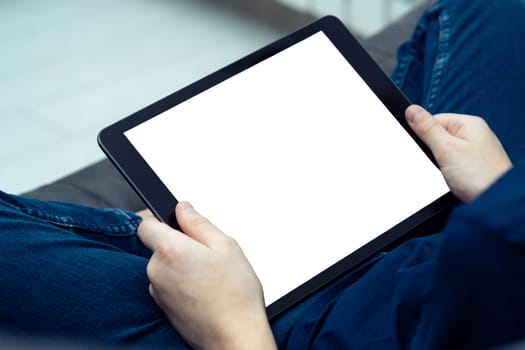 Digital tablet computer with blank white screen in male hands, from above view closeup. Young guy working on gadget at home. Tablet in hands, modern technology, touchscreen, electronics.
