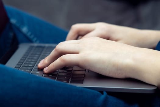 Digital laptop computer on male legs, side view closeup. Young business man typing on keyboard of portable modern notebook. Working on multitasking gadget. High technology, IT sphere, electronics.