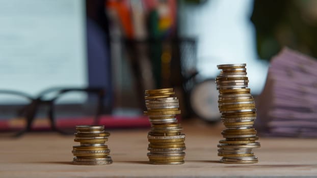 Composition of three stacks of coins near pile of papers, glasses, laptop on desk. Workspace, business technology, document, money, banking investment, information, finance, management. Soft focus.