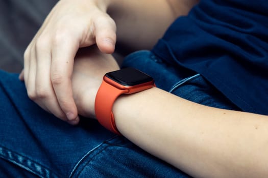 Red stylish smart watch on male wrist closeup. Young business man touch finger on empty screen of wearable gadget to look time and data. Multitasking watch, touchscreen, modern electronics.