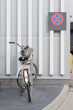 parked bicycle at a supermarket, behind it a no stopping sign on the wall