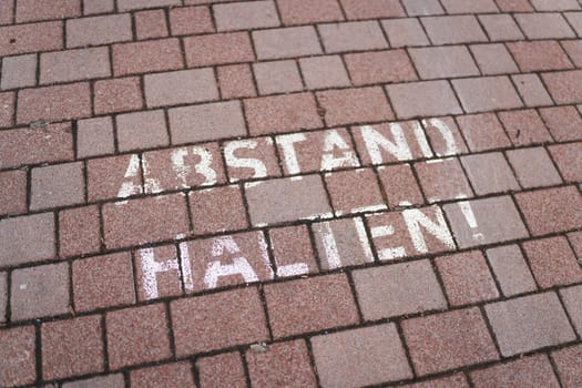 Writing on the sidewalk of a small German town during the Corona Pandemic with the words Abstand halten. Translation: keep your distance