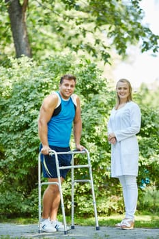 Young doctor in uniform and her patient with walker looking at camera in park