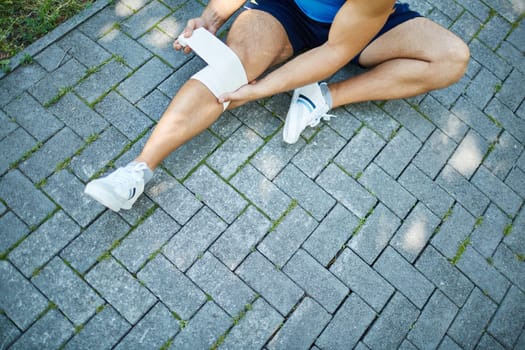 Close-up of male sitting on pavement and bandaging his knee