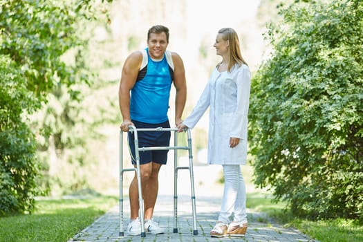 Female clinician and young man with walker taking walk in park