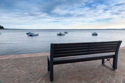 empty bench overlooking Lake Garda and boats