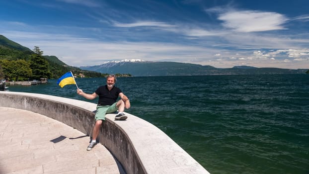 Lake Garda Italy. happy man with a flag of Ukraine against the backdrop of emerald water
