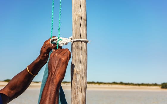 Local Malagasy man securing sail rope to a wooden pole of his ship, detail to hands only.