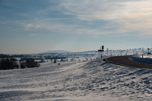 Lonely country road in winter with snow, bright sun, trees and blue sky, in the high Rhoen, Hesse, Germany