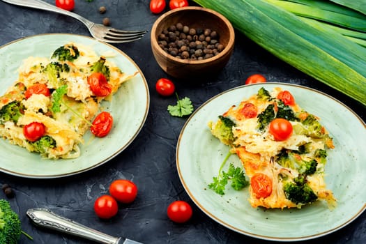 Appetizing potato casserole with broccoli and tomatoes on a plate.
