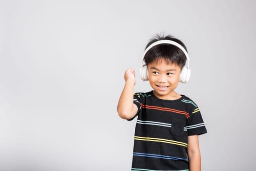 Little cute kid boy 5-6 years old listen music in wireless headphones in studio shot isolated on white background, happy Asian children smiling listening audio and dancing, entertainment lifestyle