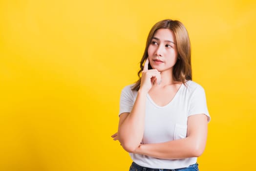 Portrait Asian Thai beautiful young woman wearing white t-shirt standing chin handle relaxed thinking about something about the question studio shot, isolated on yellow background with copy space