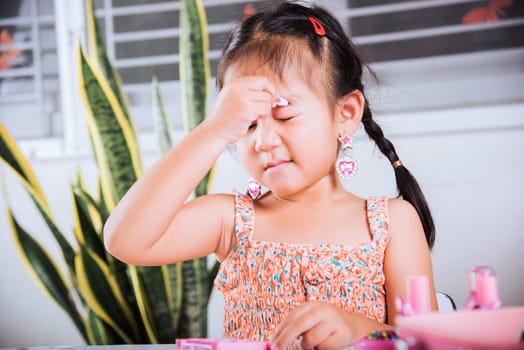 Happy kid is beautiful make up with cosmetics toy, Asian adorable funny little girl making makeup her face she applying carborundum eyeliner to eyelid, Learning activity to be woman at house