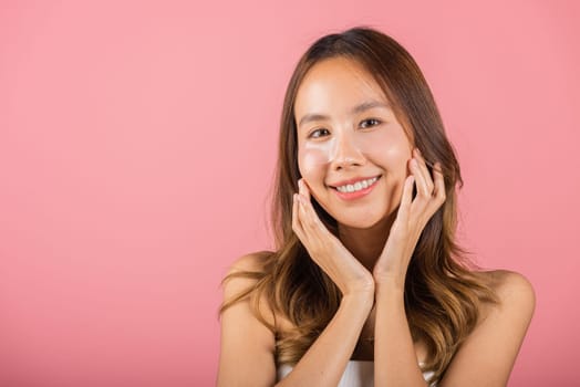 Eye skin treatment. Asian beautiful young woman smiling mask cosmetic patches gel under the eyes, Portrait female with natural makeup hydrogel eye patch on face, isolated on pink background, skincare