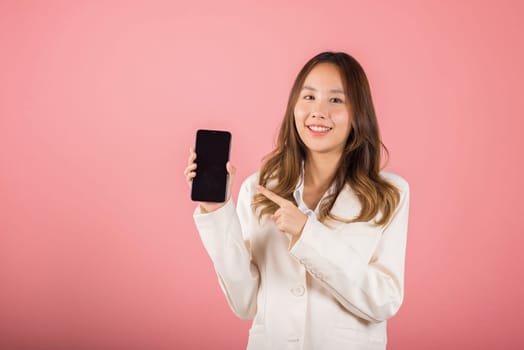 Portrait Asian happy beautiful young woman smile making finger pointing on screen smartphone in hand shopping online application looking to camera, studio shot isolated pink background with copy space