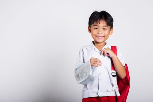 Asian student kid boy wearing student thai uniform accident broken bone wearing splint arm plaster fiberglass cast covering arm in cast at studio shot isolated on white background, back to school