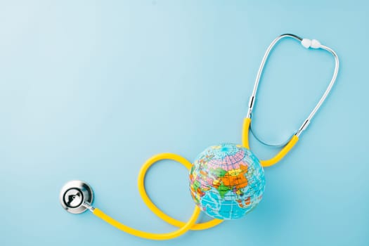 World Health Day. Top view yellow doctor stethoscope wrapped around world globe isolated on pastel blue background with copy space for text, Save world day, Health care and medical concept
