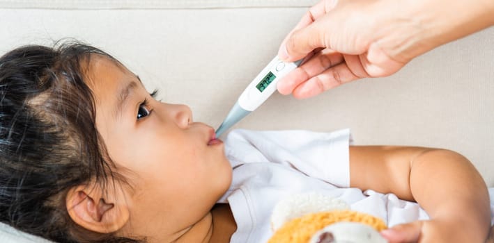 Sick kid. Mother parent checking temperature of her sick daughter with digital thermometer in mouth, child laying in bed taking measuring her temperature for fever and illness, healthcare