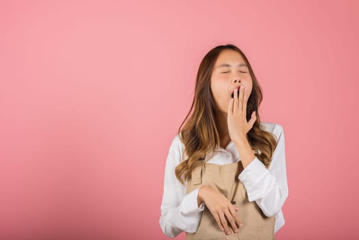 Portrait Asian beautiful young woman wearing overalls emotions tired and sleepy her yawning covering mouth open by hand, studio shot isolated on pink background, Female attractive insomnia boring