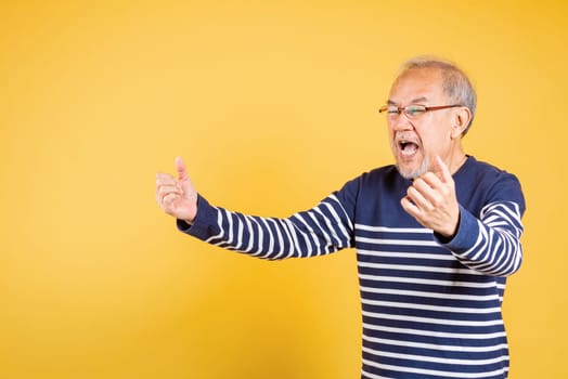 Happy Asian elder man with glasses excited say yes gesture like winner studio shot isolated on yellow background, Portrait smiling senior old man lifestyle he arms raised to celebrating his success