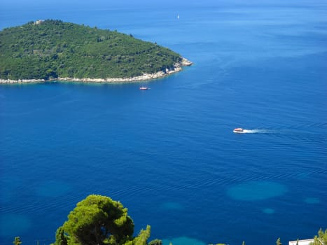 Aerial view of the Adriatic Sea. Island near Dubrovnik, Croatia. Beautiful blue sea surface with ships, boats and yachts. Light spots on the water. Pine crown and dried grass on a rocky shore.