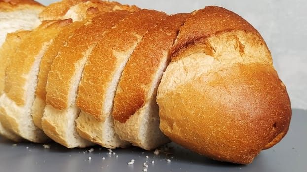 Sliced loaf of wheat flour. Appetizing slices of white bun with crispy baked crust. Product containing gluten. Fresh bread. Gray background. Crumbs on the table