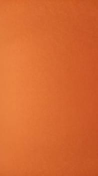 A sheet of thick paper of bright orange color. Close-up. Background intense shade. Natural lateral lighting. Fine cardboard or paper texture. Light gradient in degree of illumination. Copy space.