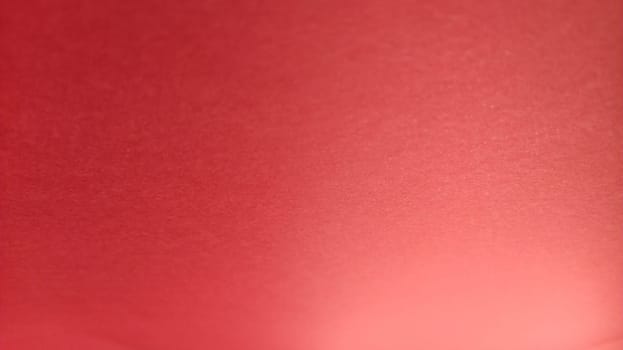 Beautiful red bright background. Color gradient depending on the lighting. Scarlet uneven color. A sheet of colored paper with natural light. Fragment of a sheet of colored paper with a glare of light