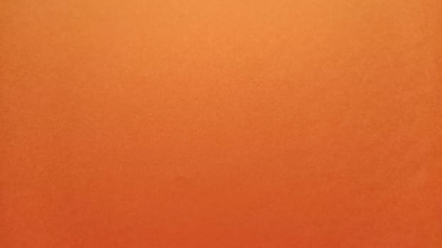 A sheet of thick paper of bright orange color. Close-up. Background intense shade. Natural lateral lighting. Fine cardboard or paper texture. Light gradient in degree of illumination. Copy space.