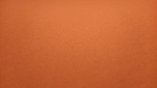 A sheet of thick paper of bright orange color. Close-up. Background intense shade. Natural lateral lighting. Fine cardboard or paper texture. Light gradient in degree of illumination. Copy space.