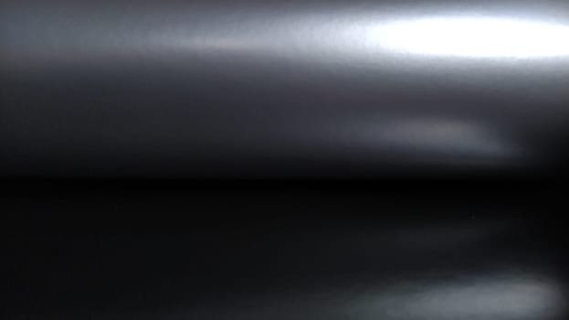 Gradient on a gray-black background. Horizontally folded shiny paper or foil with overflow and highlights. Mysterious radiance. Luxurious fabric. Metallic cold shine