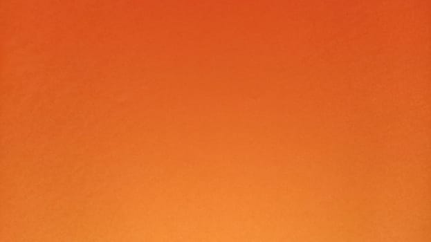 A sheet of thick paper of bright orange color. Close-up. Background intense shade. Natural lateral lighting. Fine cardboard or paper texture. Light gradient in degree of illumination. Copy space