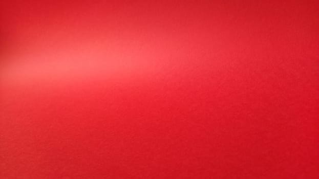 Beautiful red bright background. Color gradient depending on the lighting. Scarlet uneven color.A sheet of colored paper with natural light. Fragment of a sheet of colored paper with a glare of light.
